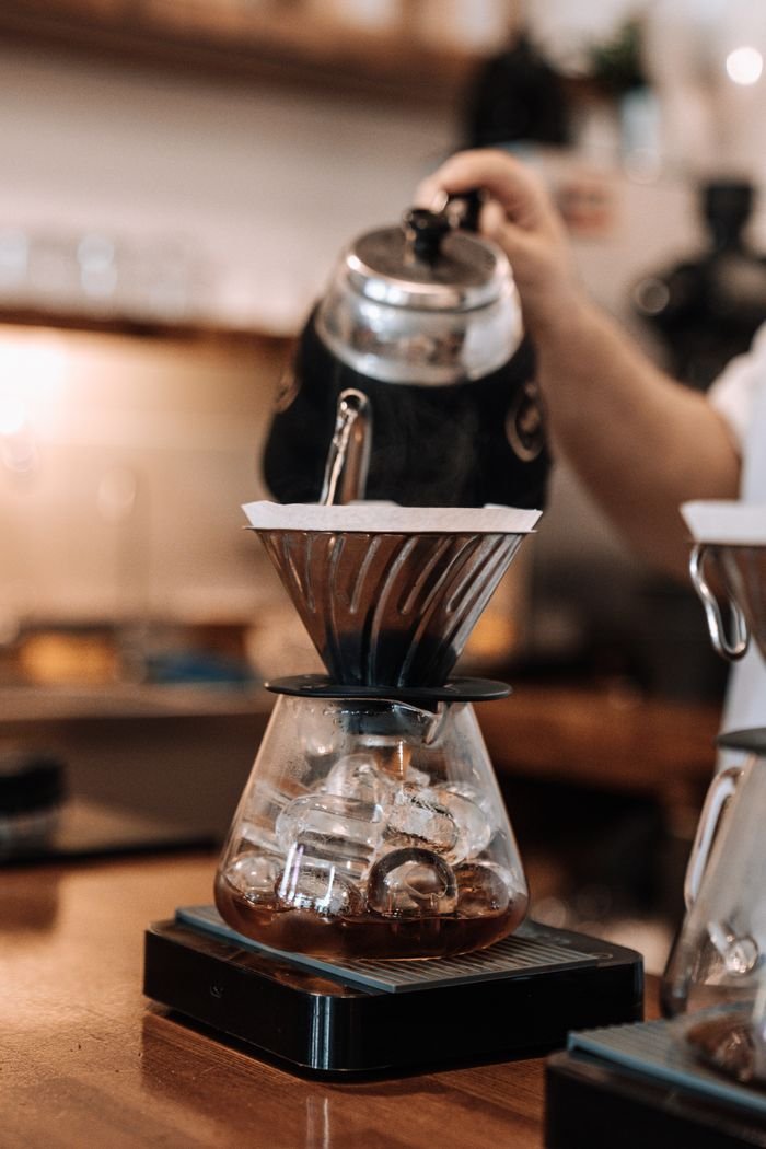 Close-up of water being poured into a coffee dripper in a cozy cafe setting.
